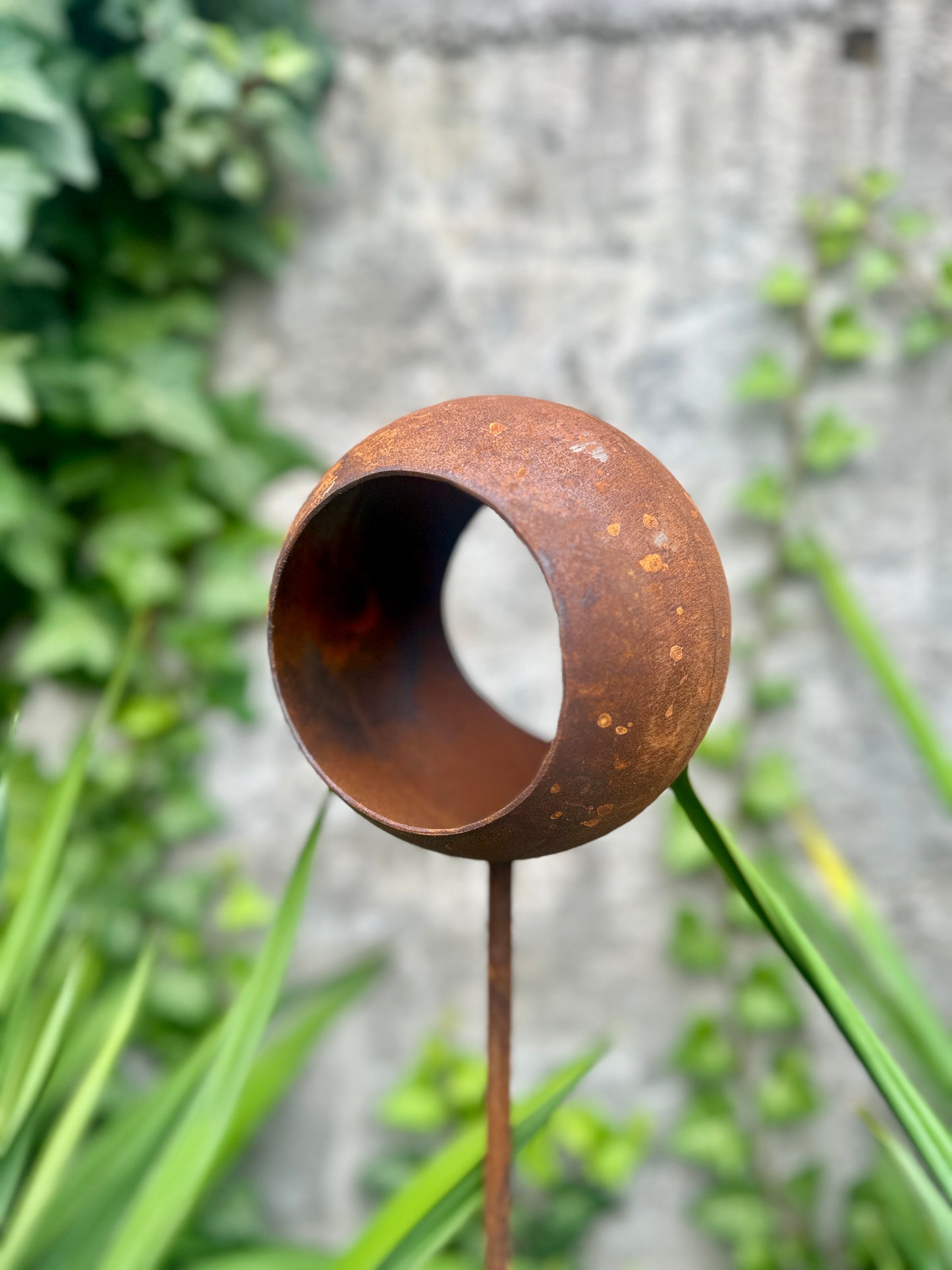Rust-colored metal garden stake with a circular design in a garden setting