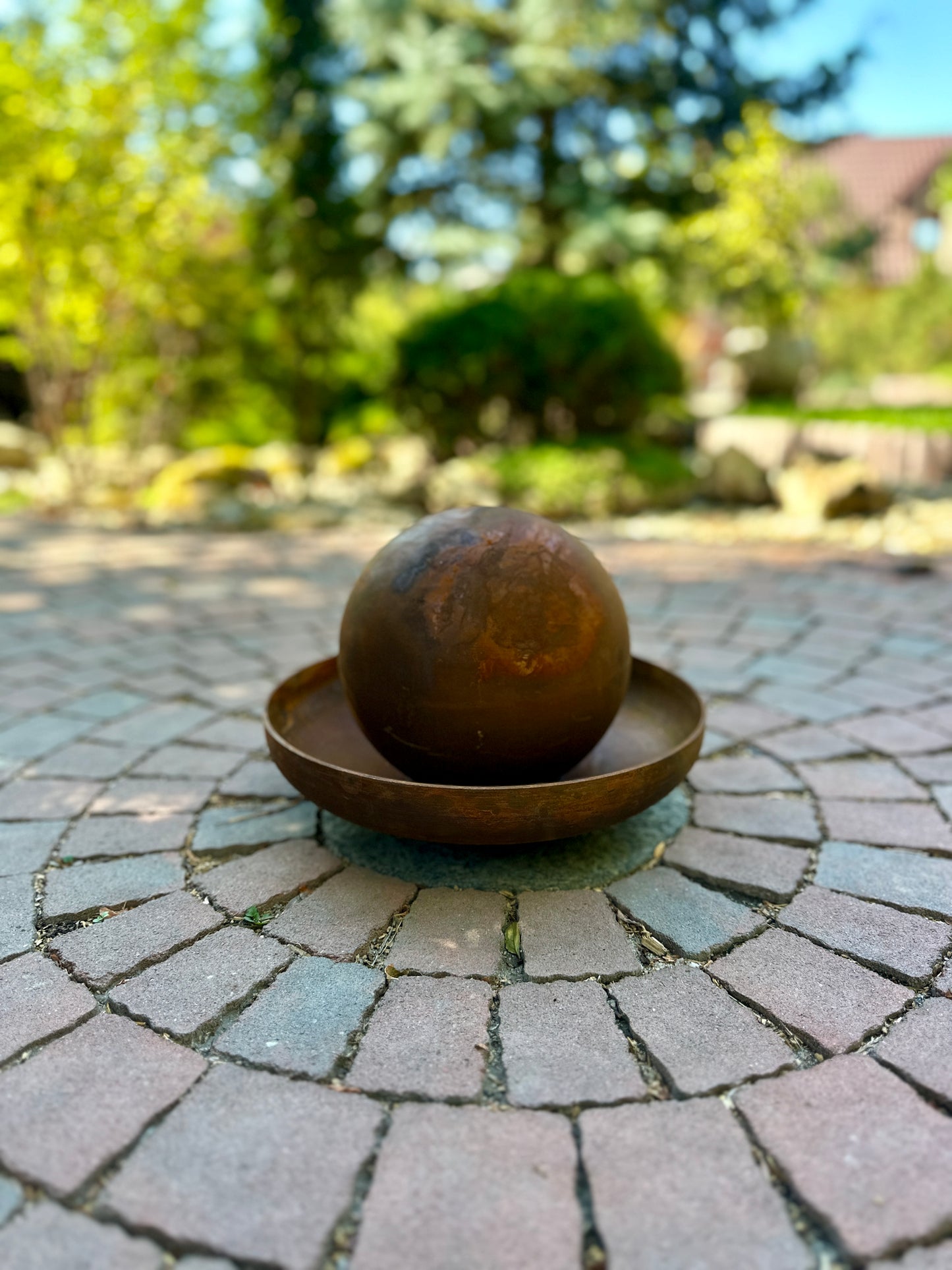 Decorative metal ball on a stone patio with greenery in the background