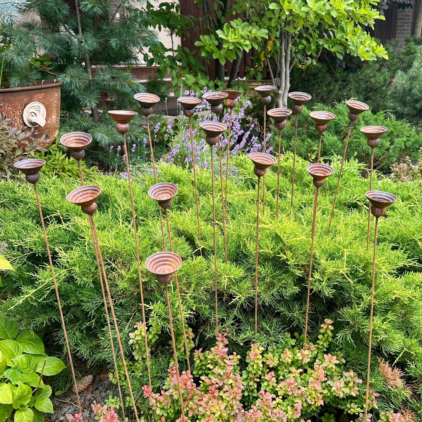 Decorative metal garden stakes in a garden setting with greenery and a house in the background.