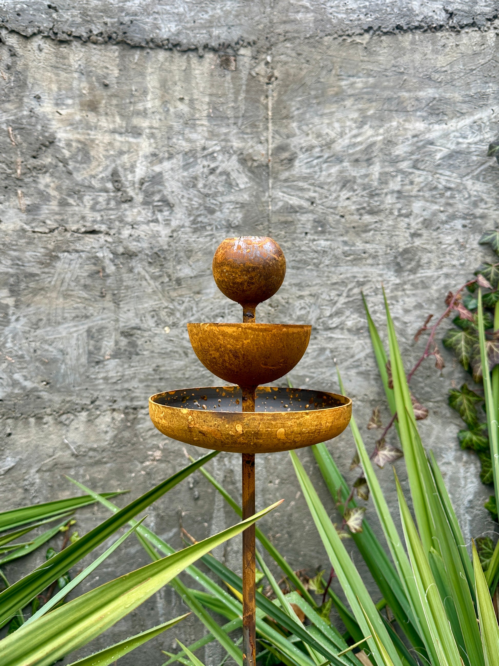 Rusty metal rain catchers, bird baths, bird feeder.