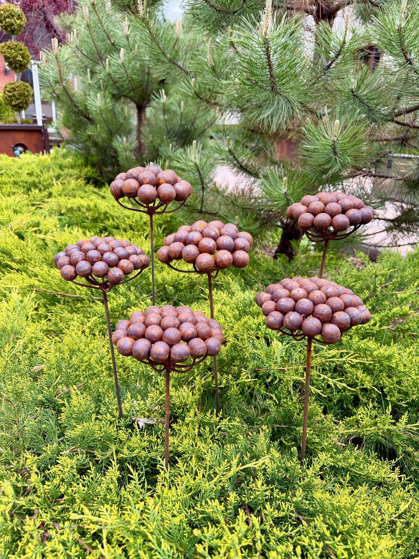 Decorative metal sculptures resembling flowers in a garden setting with trees and shrubs.