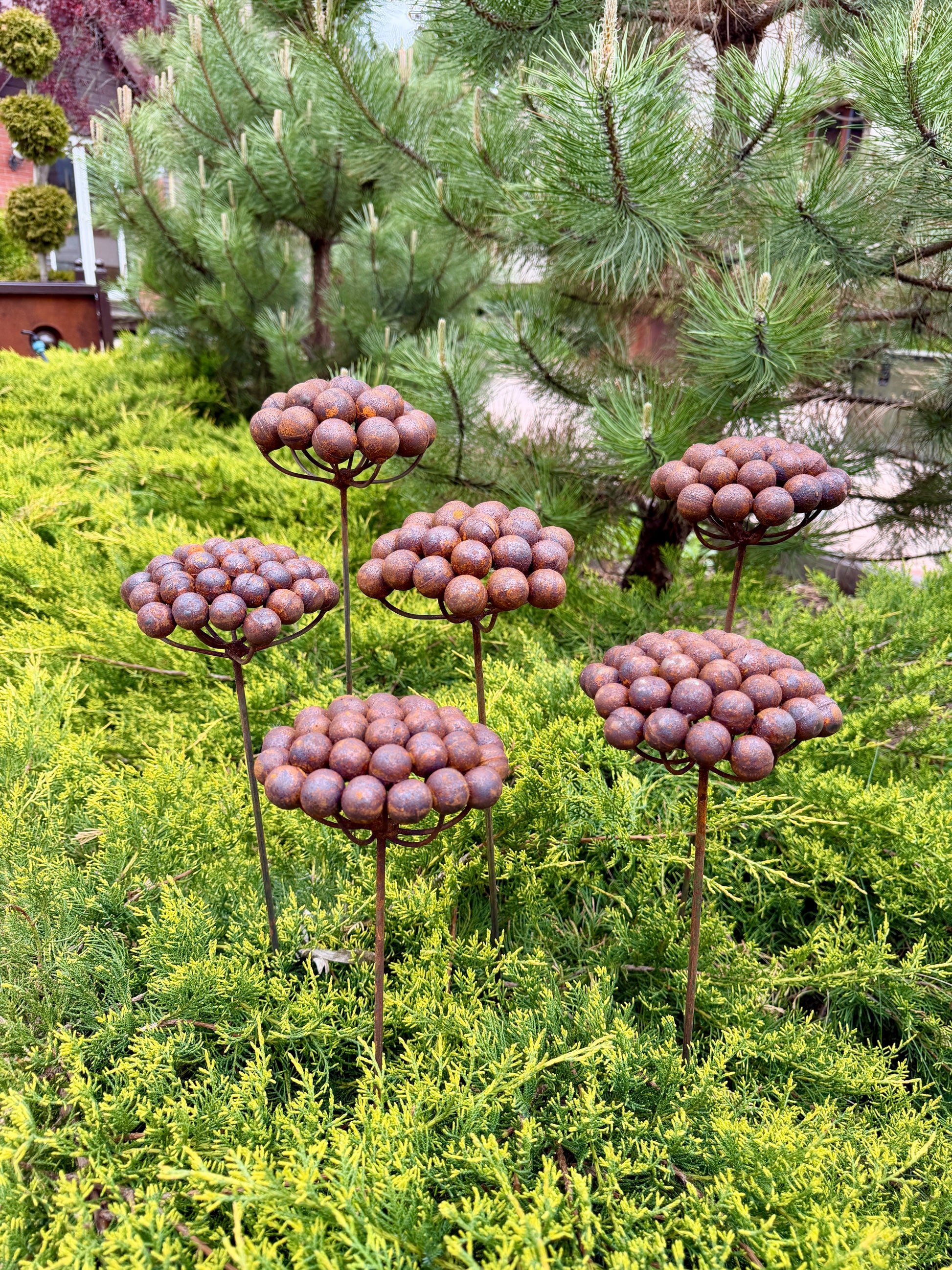 Decorative metal sculptures resembling flowers in a garden setting with trees and shrubs.