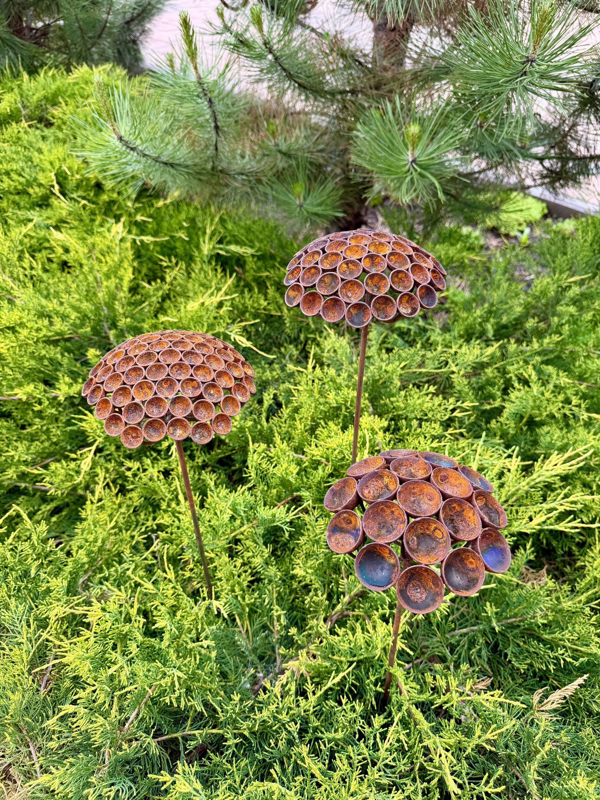 Three decorative metal flower sculptures in front of green foliage