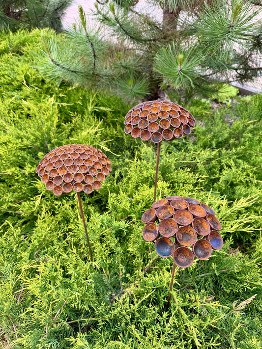 Three decorative metal flower sculptures in front of green foliage