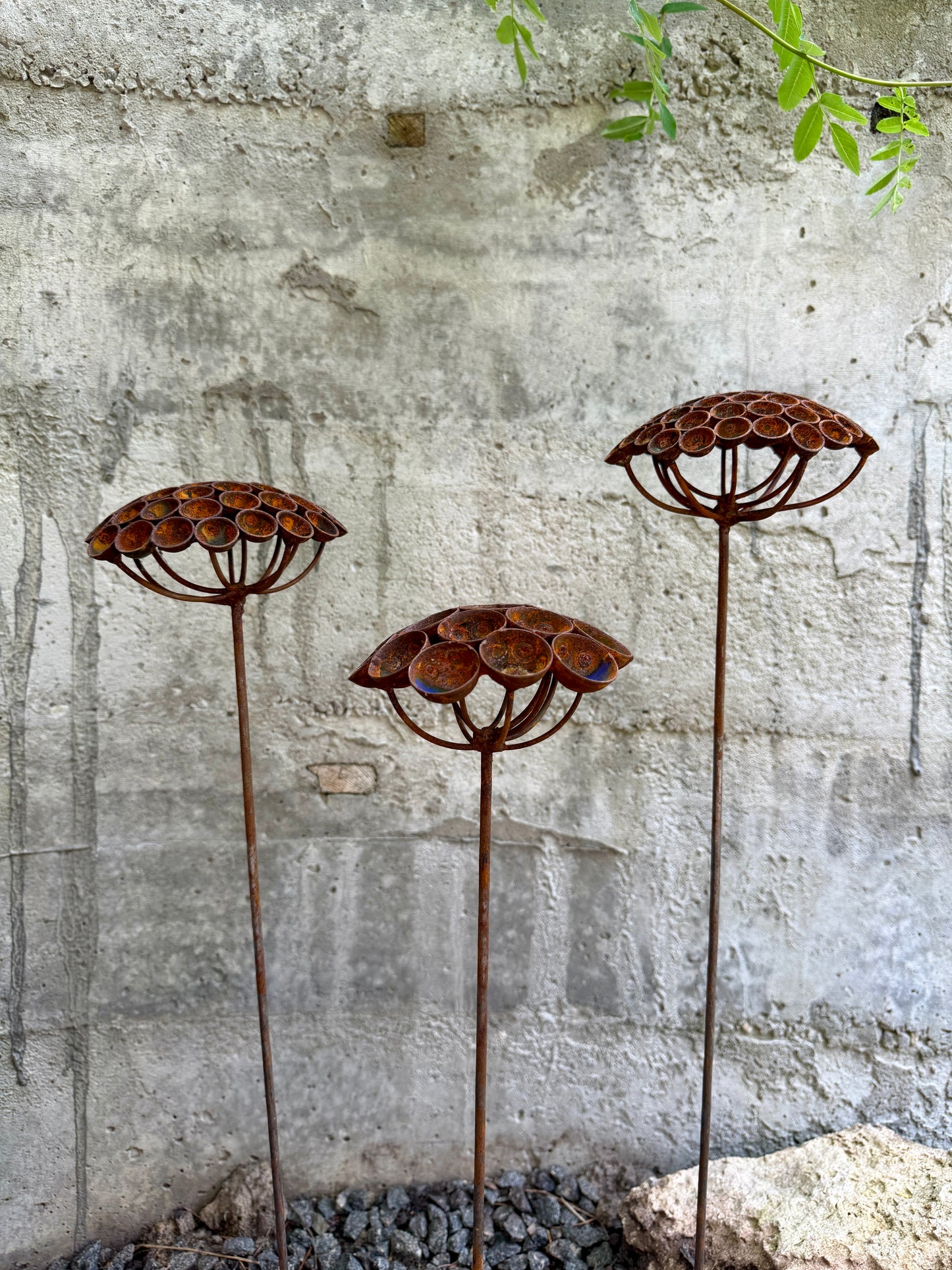 Three rusted metal garden art pieces against a textured wall.