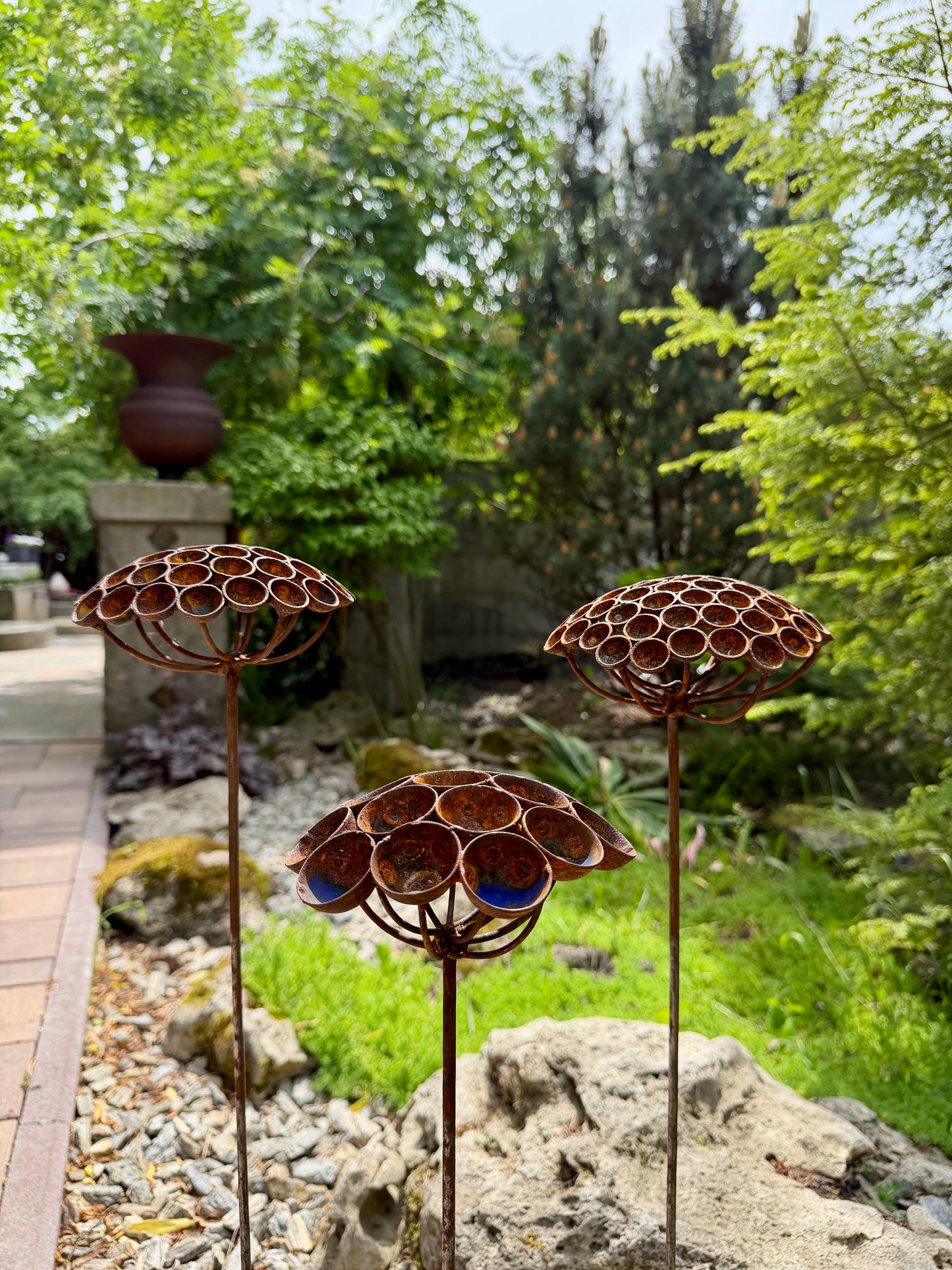 Decorative metal flower sculptures in a garden setting with greenery and rocks.