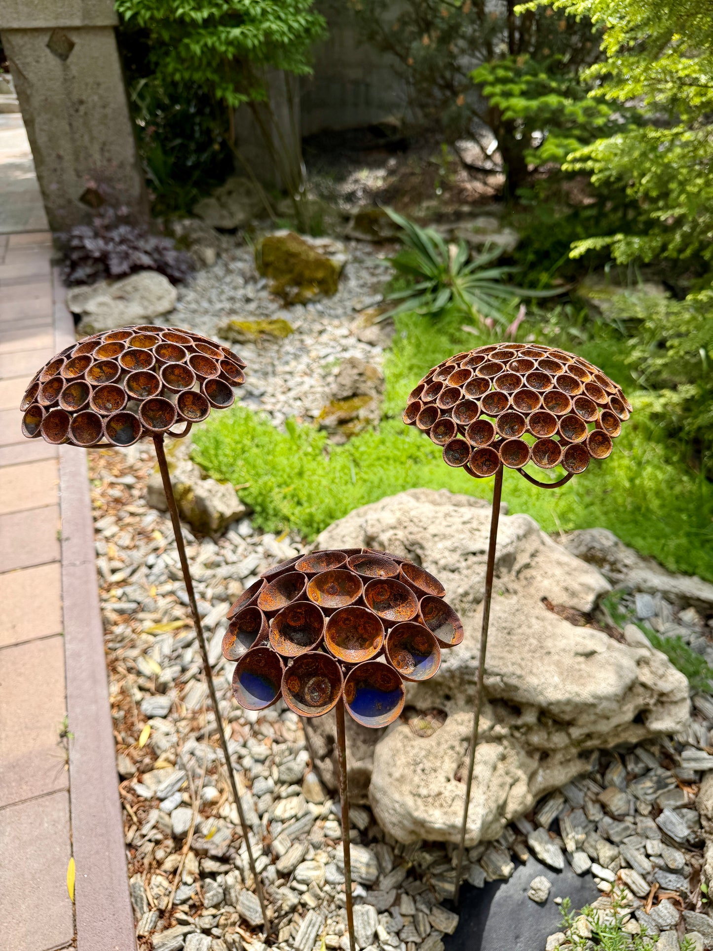 Metal garden art resembling beehives in a garden setting with rocks and plants.
