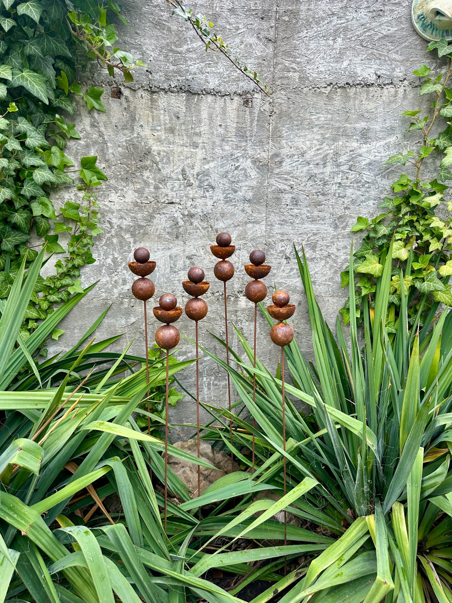 Decorative metal stakes with spherical ends in a garden setting.