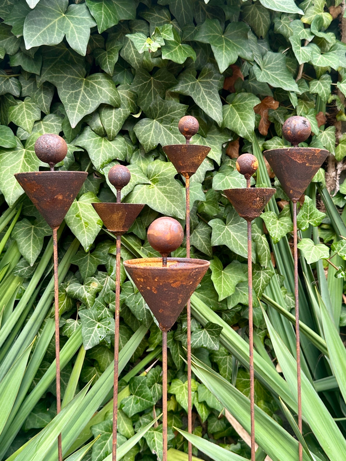 Decorative metal garden stake with funnel-shaped top against a green leafy background
